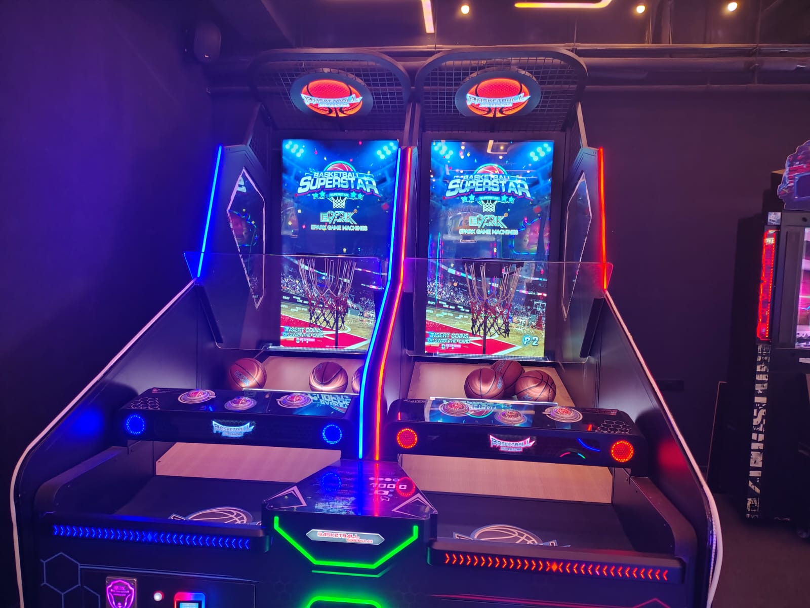 Two arcade basketball games are set up side-by-side in a dimly lit entertainment venue.