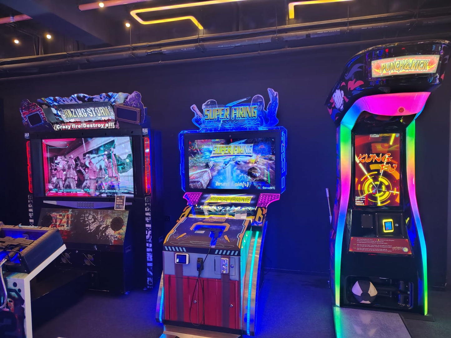 Arcade with three colorful, illuminated video game cabinets: "Crazy Storm," "Super Firing," and "Punch & Kick."
