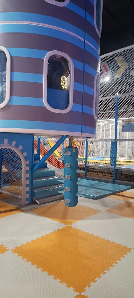 A colorful indoor playground with a blue and gray tower, slides, and trampolines.