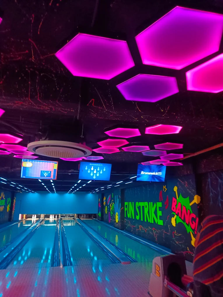 A neon-lit bowling alley with hexagonal purple lights on the ceiling and "FUN STRIKE BANG!" graffiti on the wall.