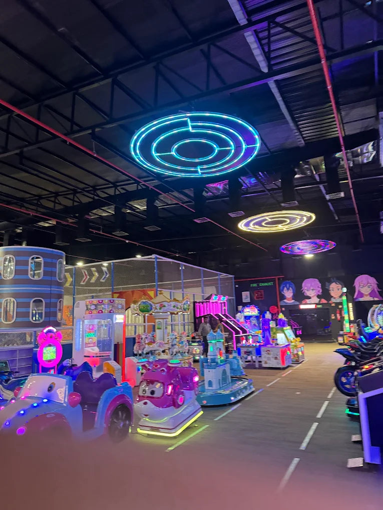 An indoor arcade with colorful rides and games, featuring neon lights and anime-style decorations.