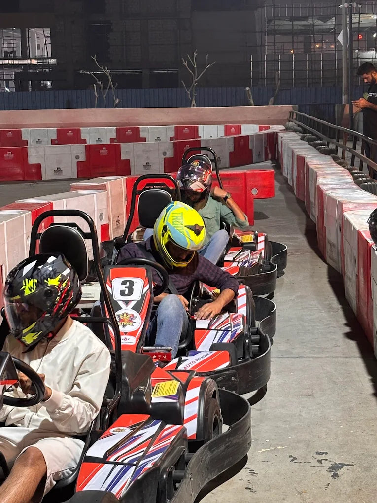 Young adults in helmets race go-karts on an indoor track at night.