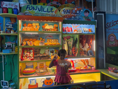 A young girl holds a basket of eggs in front of a colorful play bakery and fish market.