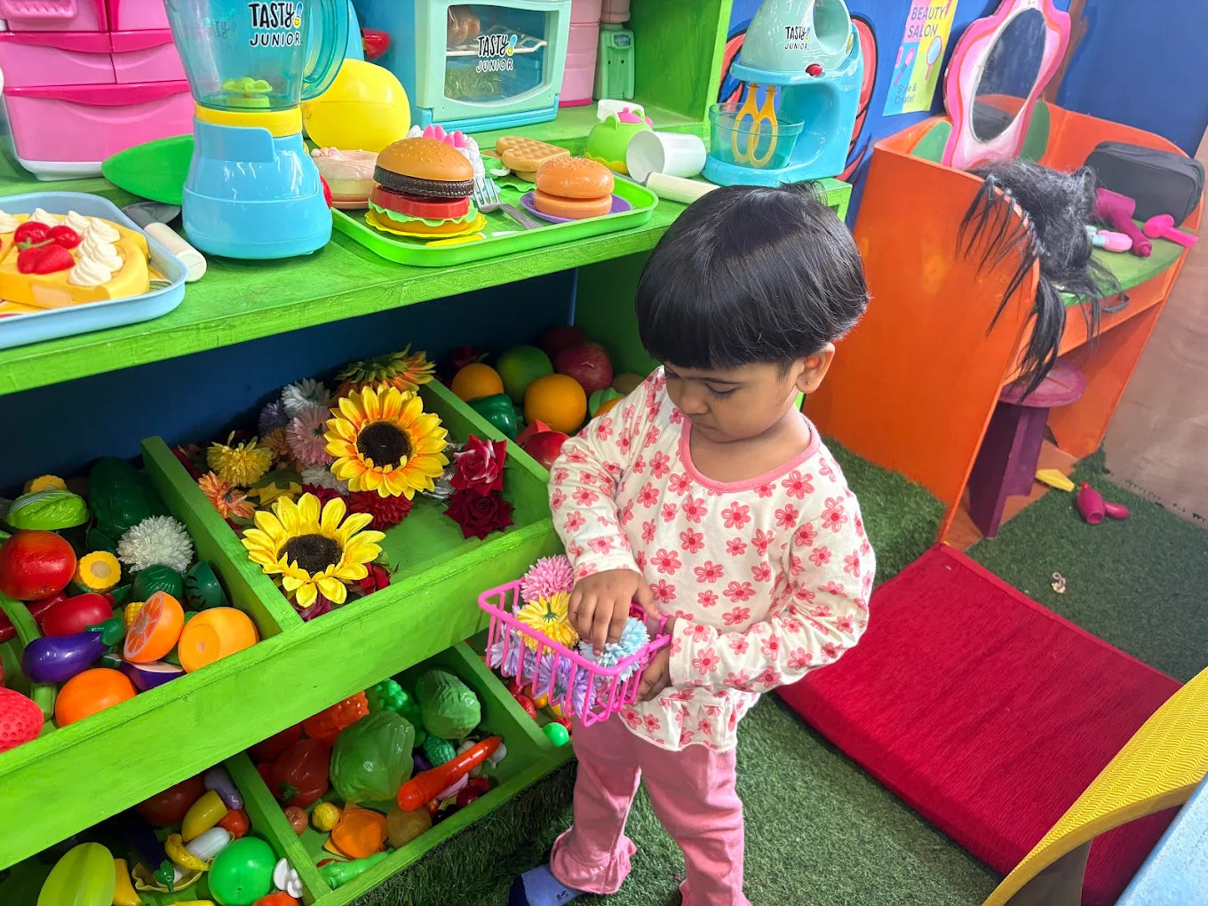 A young child plays with toy food in a colorful play kitchen and salon setting.