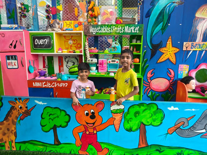 Two young boys stand in front of a colorful play kitchen and market, with painted animals and sea creatures on the backdrop.