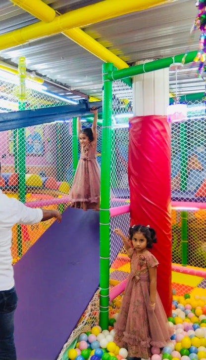 Two young girls play in a colorful indoor playground with a ball pit.