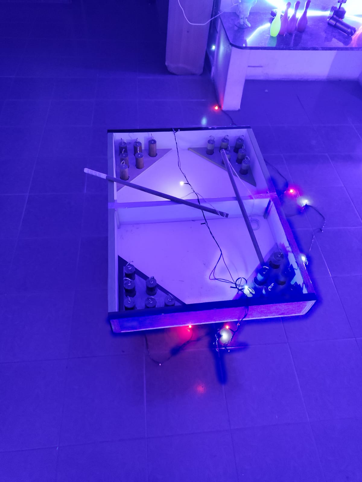 A handmade bowling game with small pins and cues, decorated with colorful lights, sits on a tiled floor.