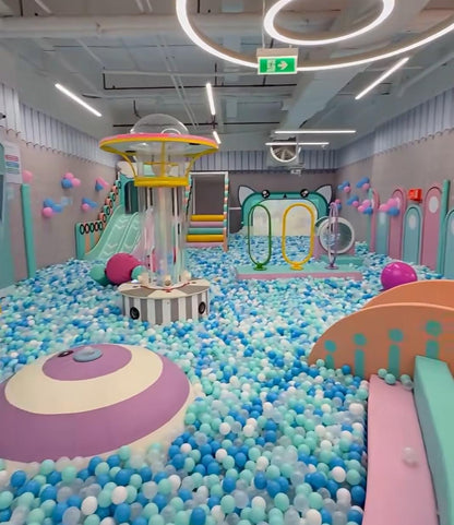A colorful indoor playground filled with blue and white balls, featuring slides and play structures for children.