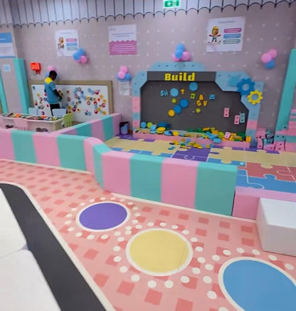 A colorful indoor play area for children with a "Build" station and soft play elements.