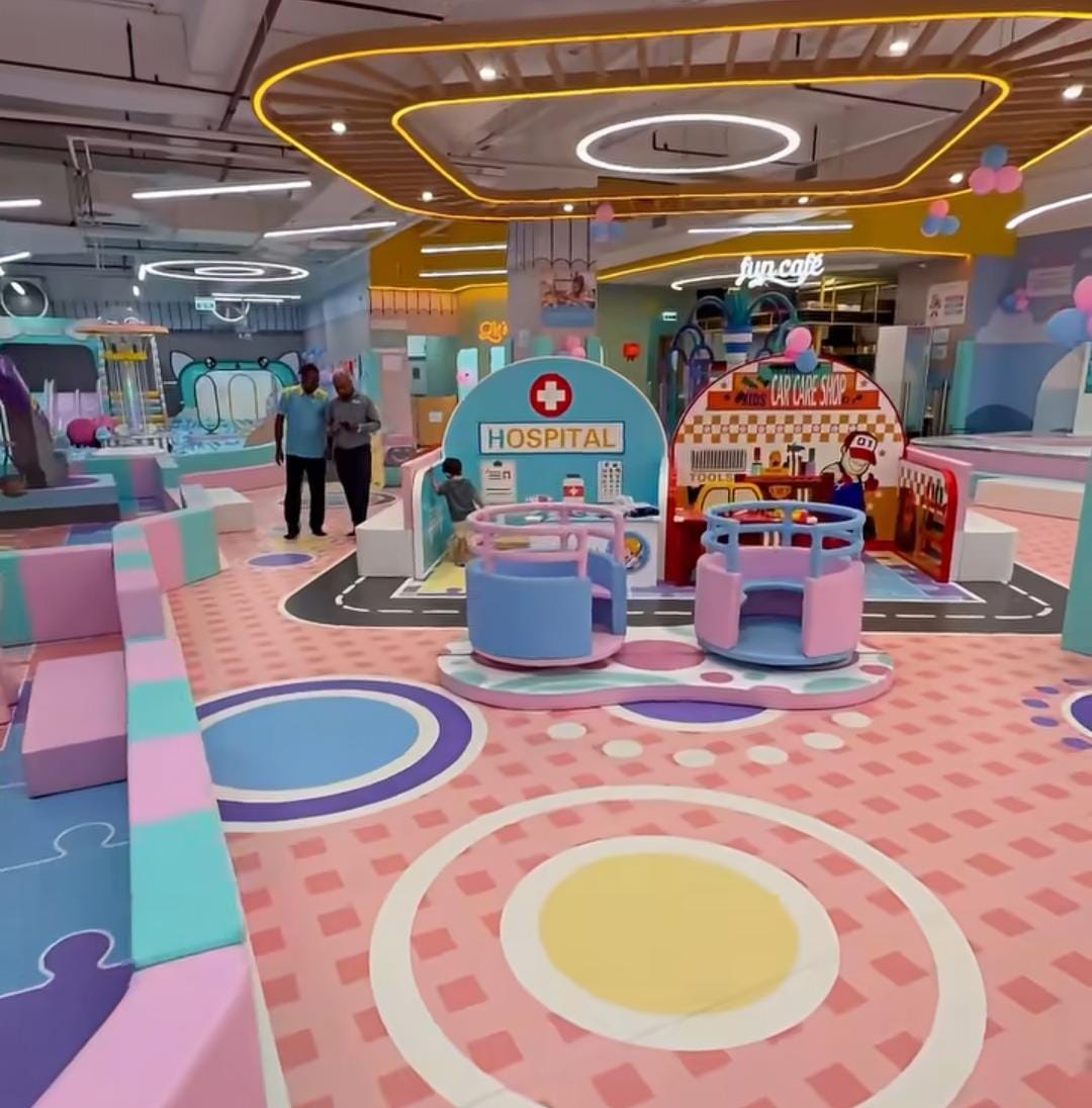 A colorful indoor playground with children playing at a pretend hospital and car wash.