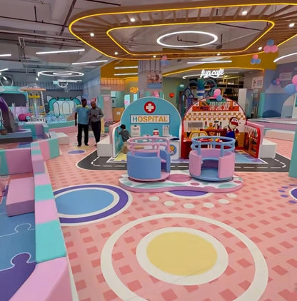 A colorful indoor playground with children playing at a pretend hospital and car wash.
