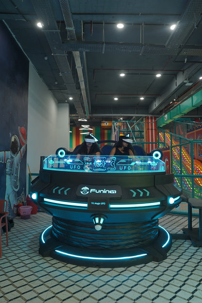 Two young people wearing VR headsets play a virtual reality game on a futuristic UFO-themed ride.