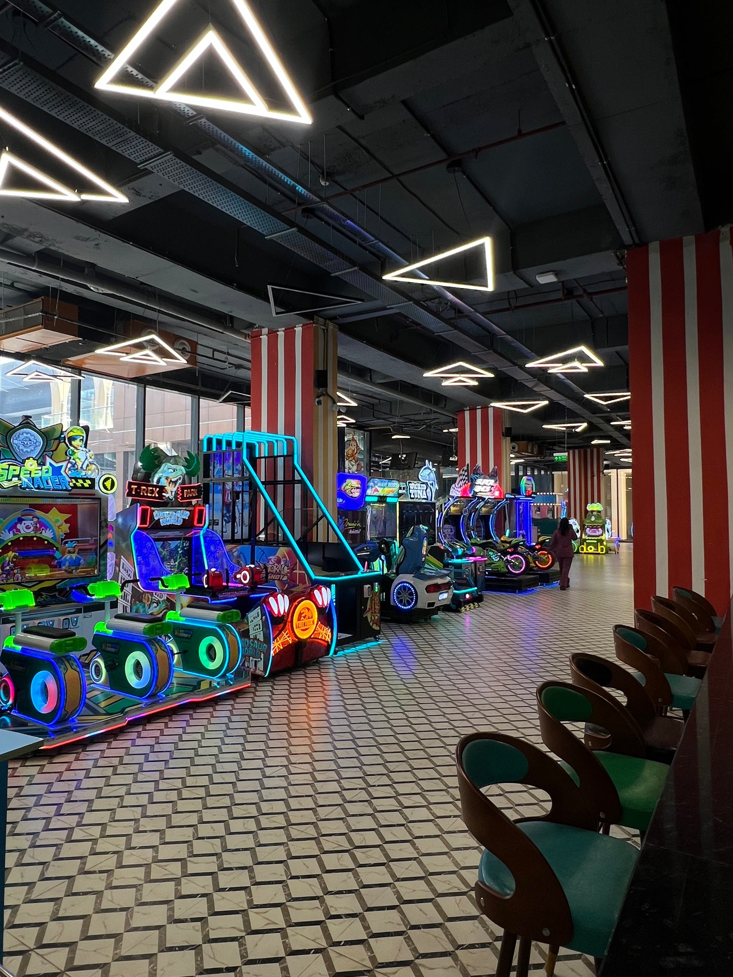 An arcade with rows of colorful racing games and a person walking away.