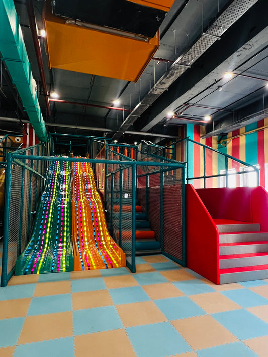 A colorful indoor playground with a large slide and stairs for children. The slide is lit with colorful LED lights.