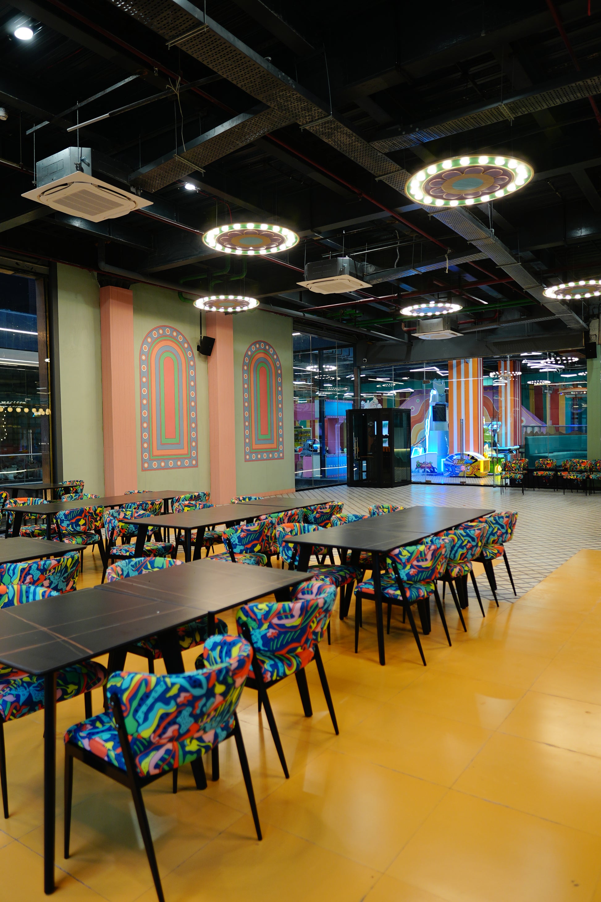A brightly colored dining area with tables and chairs, featuring abstract patterns. The space appears to be part of an entertainment venue.