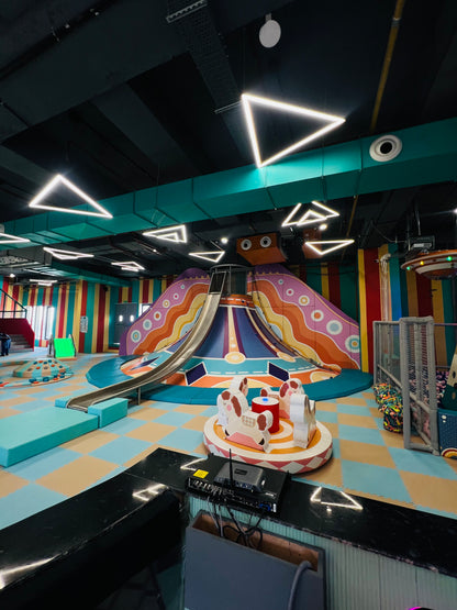 A colorful indoor playground with slides, a carousel, and soft play areas for children.