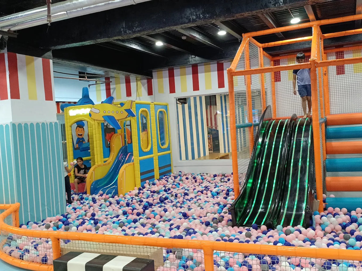 Children play in a colorful indoor playground with a ball pit and slides.