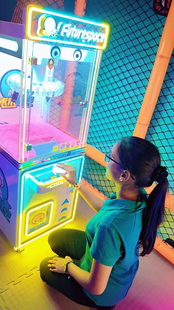 A young woman plays a brightly lit claw machine in an arcade.