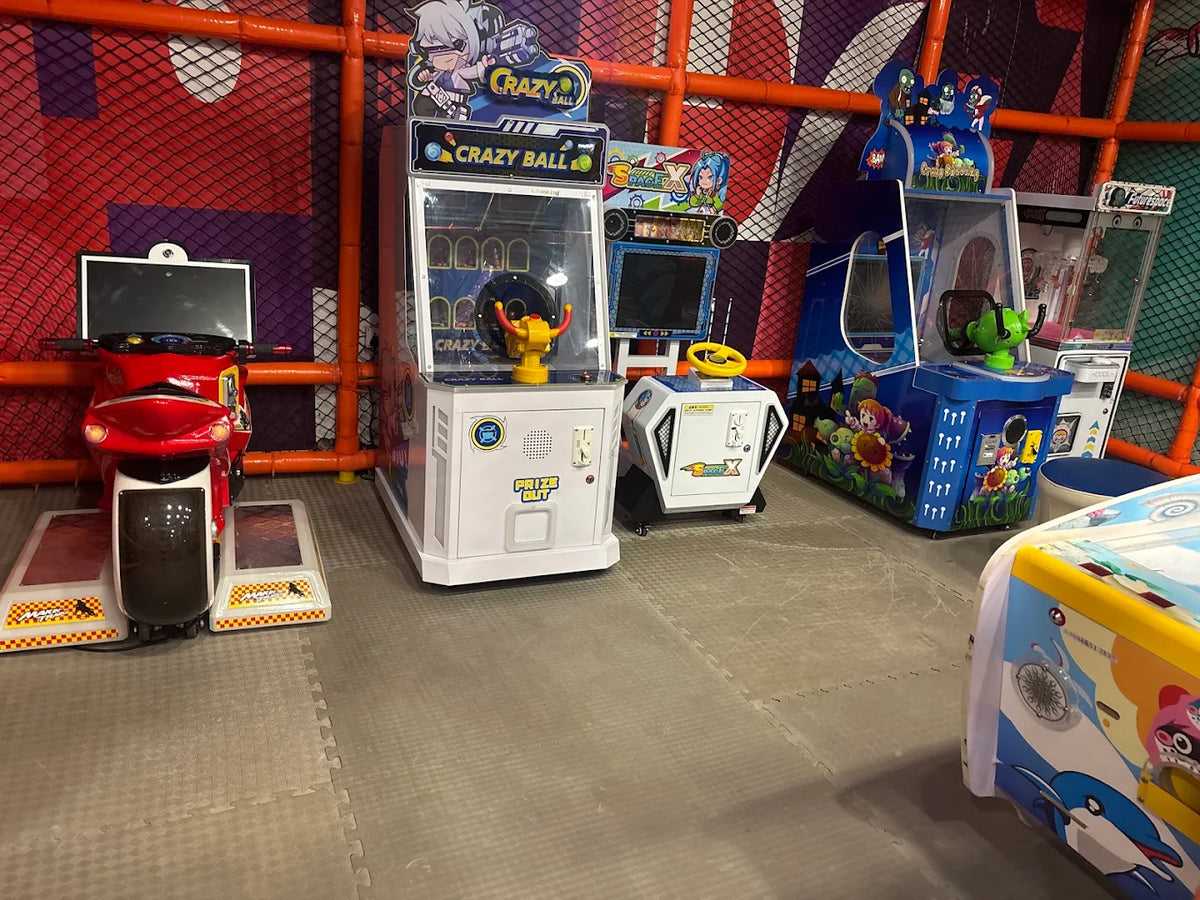 Arcade games, including a motorcycle ride and prize machines, are set up in a colorful indoor play area for children.
