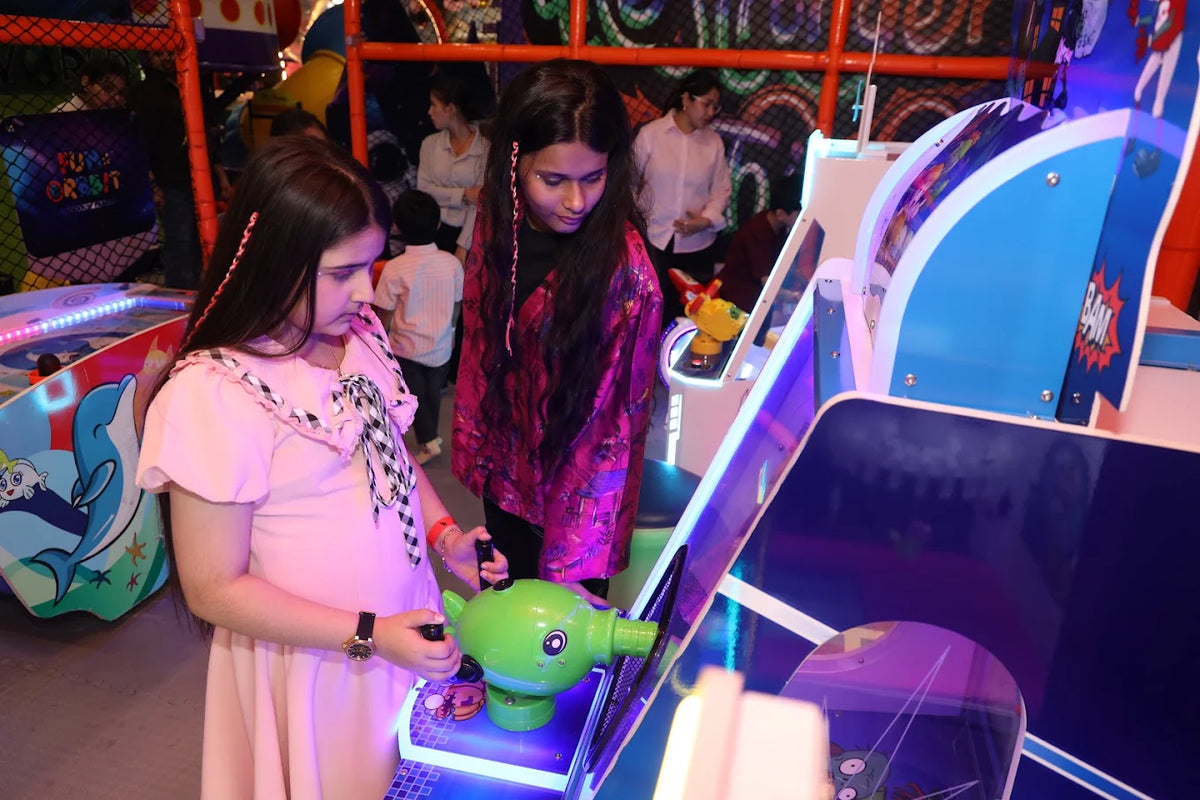 Two young girls play an arcade game in a brightly lit entertainment center.