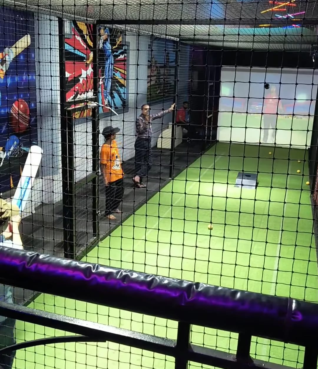 People in a cricket batting cage with a projection screen.