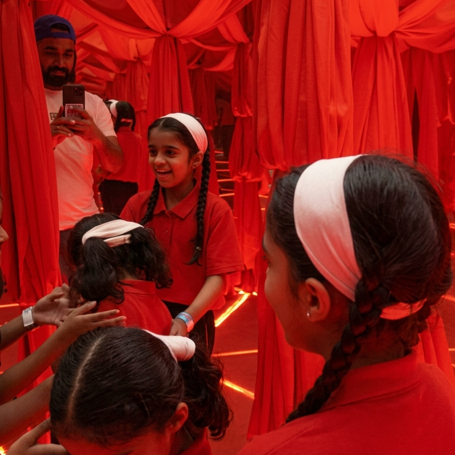Children in red shirts and headbands interact in a room with red draped fabric.