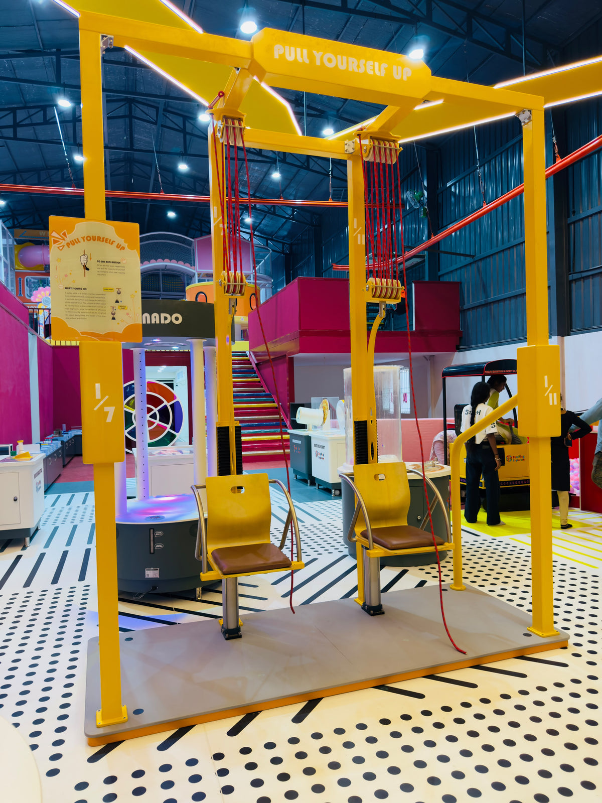 A yellow pulley system with two seats is set up in an indoor play area for children.