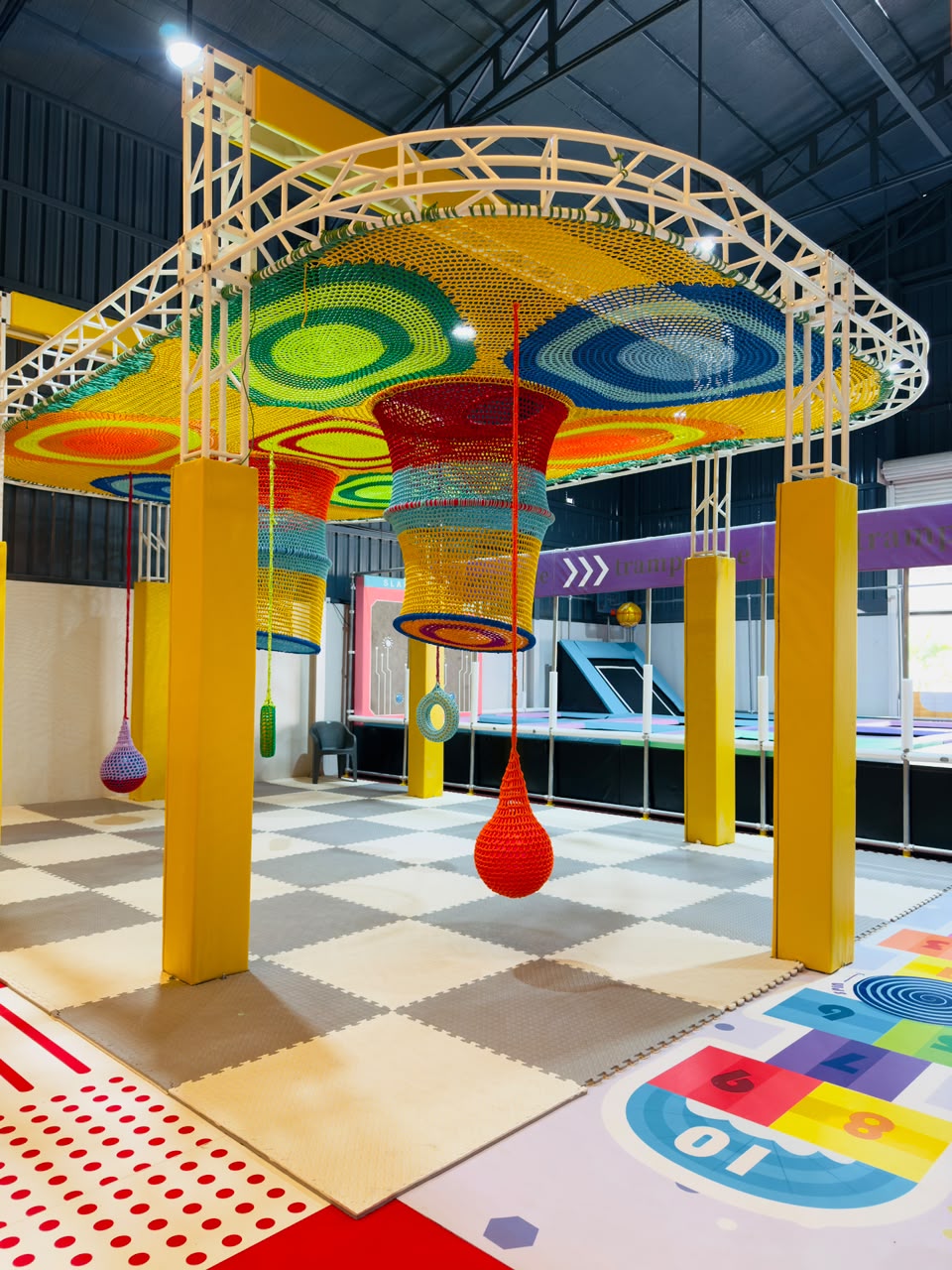 Indoor playground with colorful nets, hanging punching bags, and foam floor mats for children.