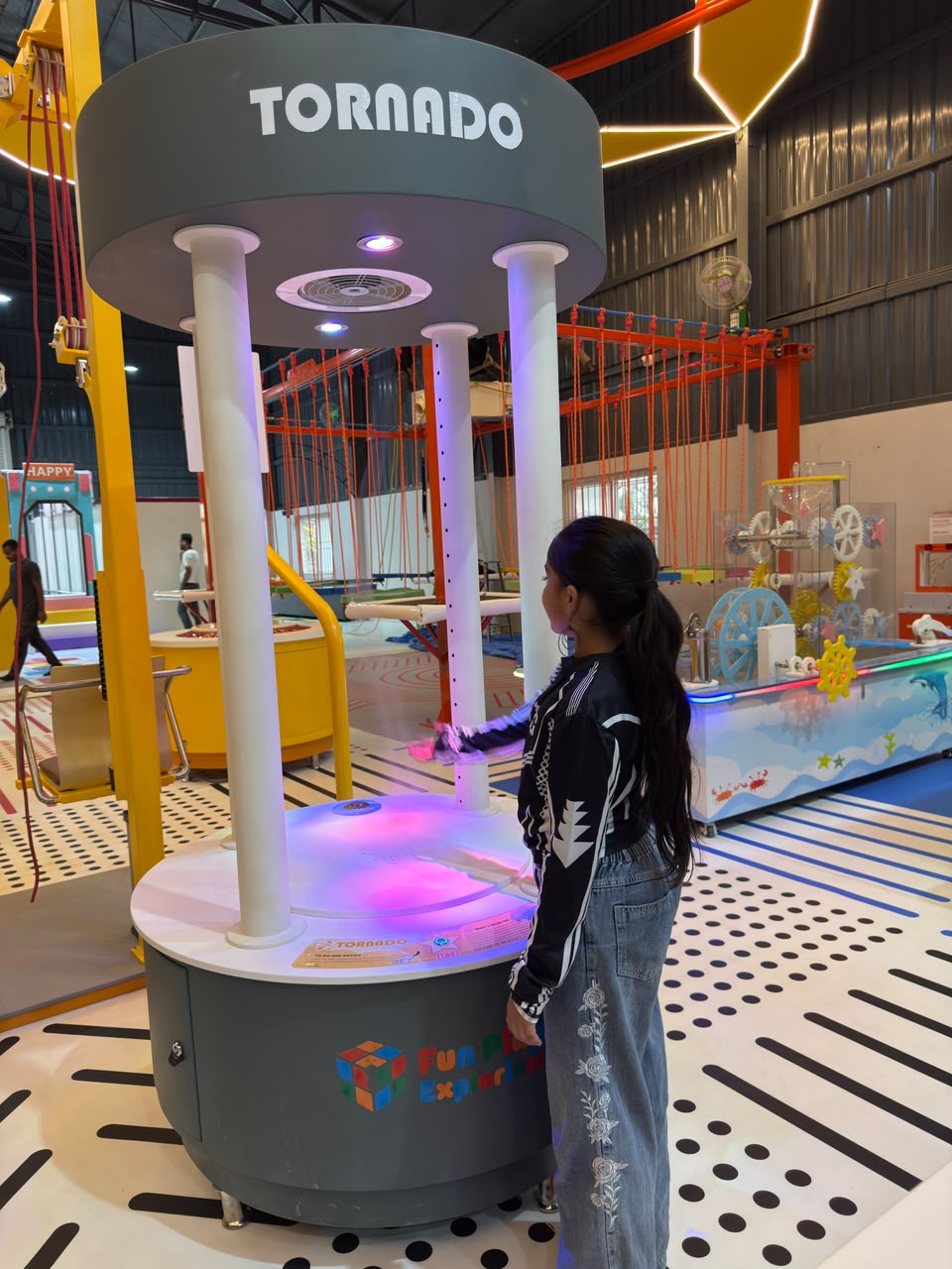 A young person interacts with a "Tornado" exhibit at an indoor play center.