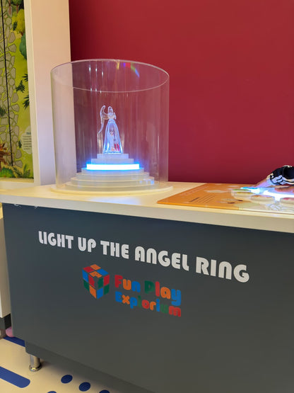 A child's hand interacts with a light-up display featuring an angel figurine in a museum exhibit.