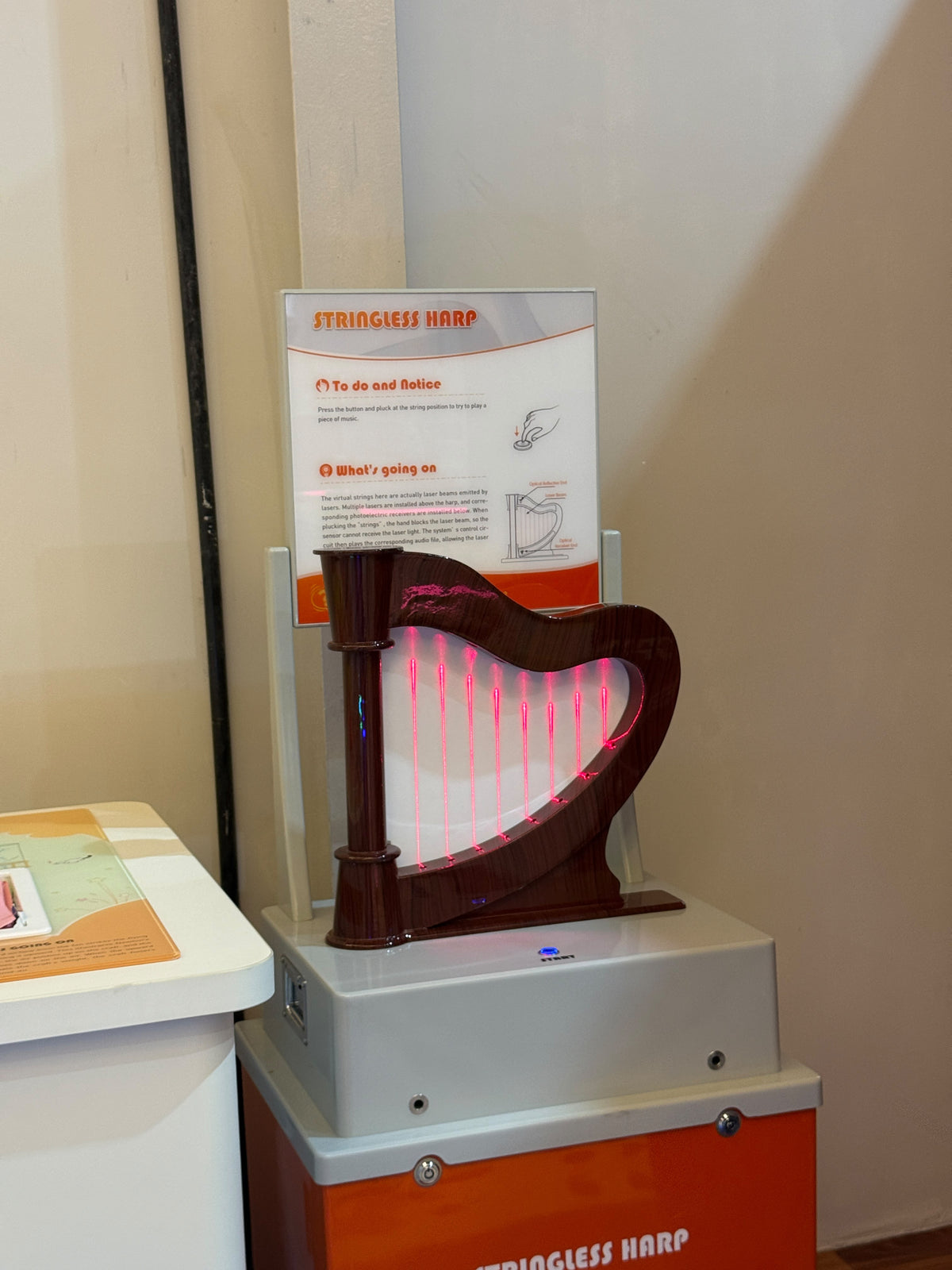 A stringless harp with glowing pink laser "strings" is displayed in an exhibit. Instructions explain how to play the virtual instrument.