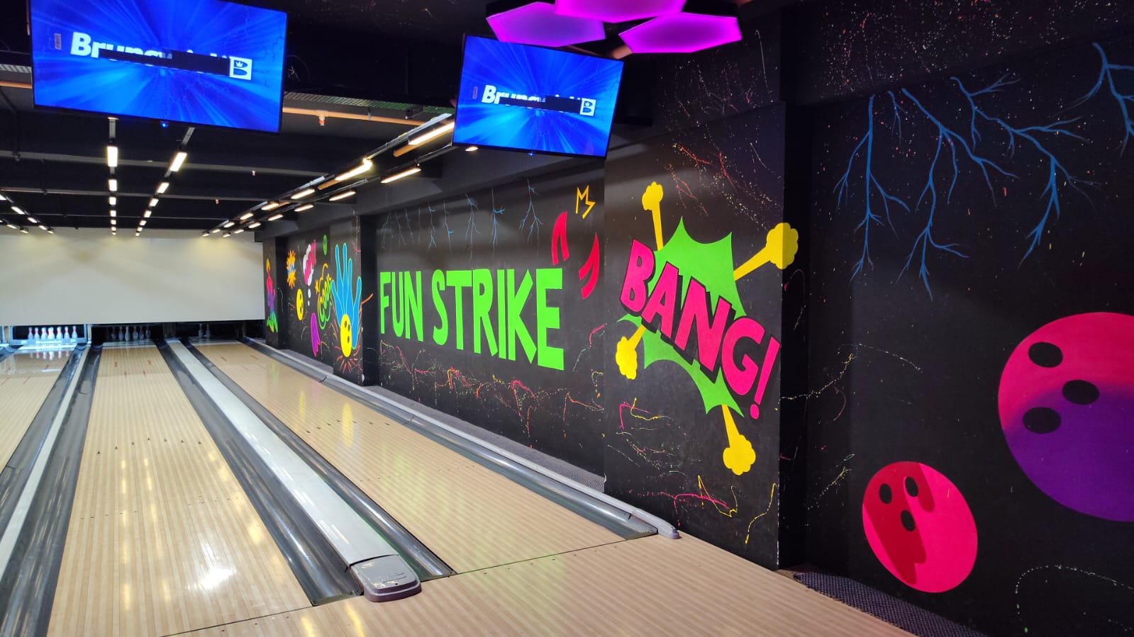 A bowling alley with neon graffiti and screens displaying "Brunswick".