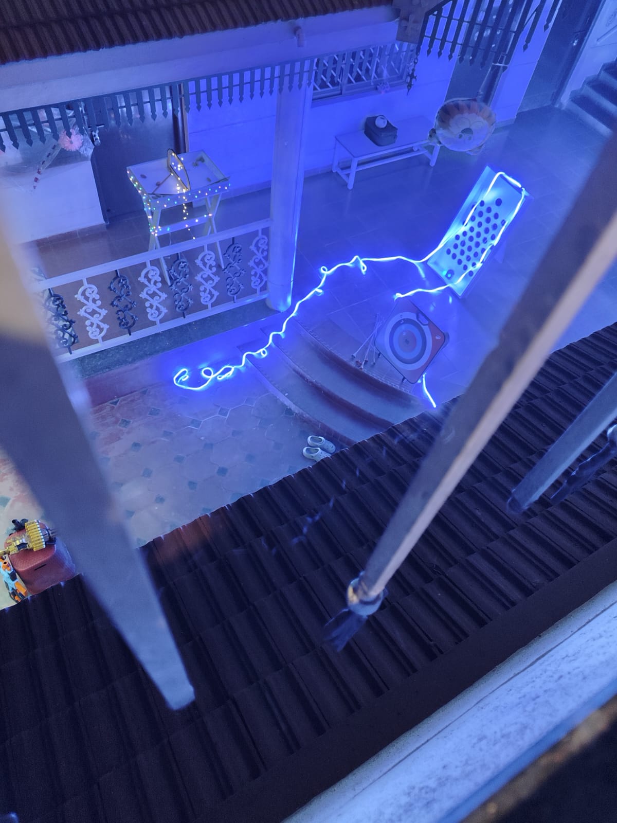 A neon blue light installation in the shape of a phone and a wire decorates an outdoor patio at night.