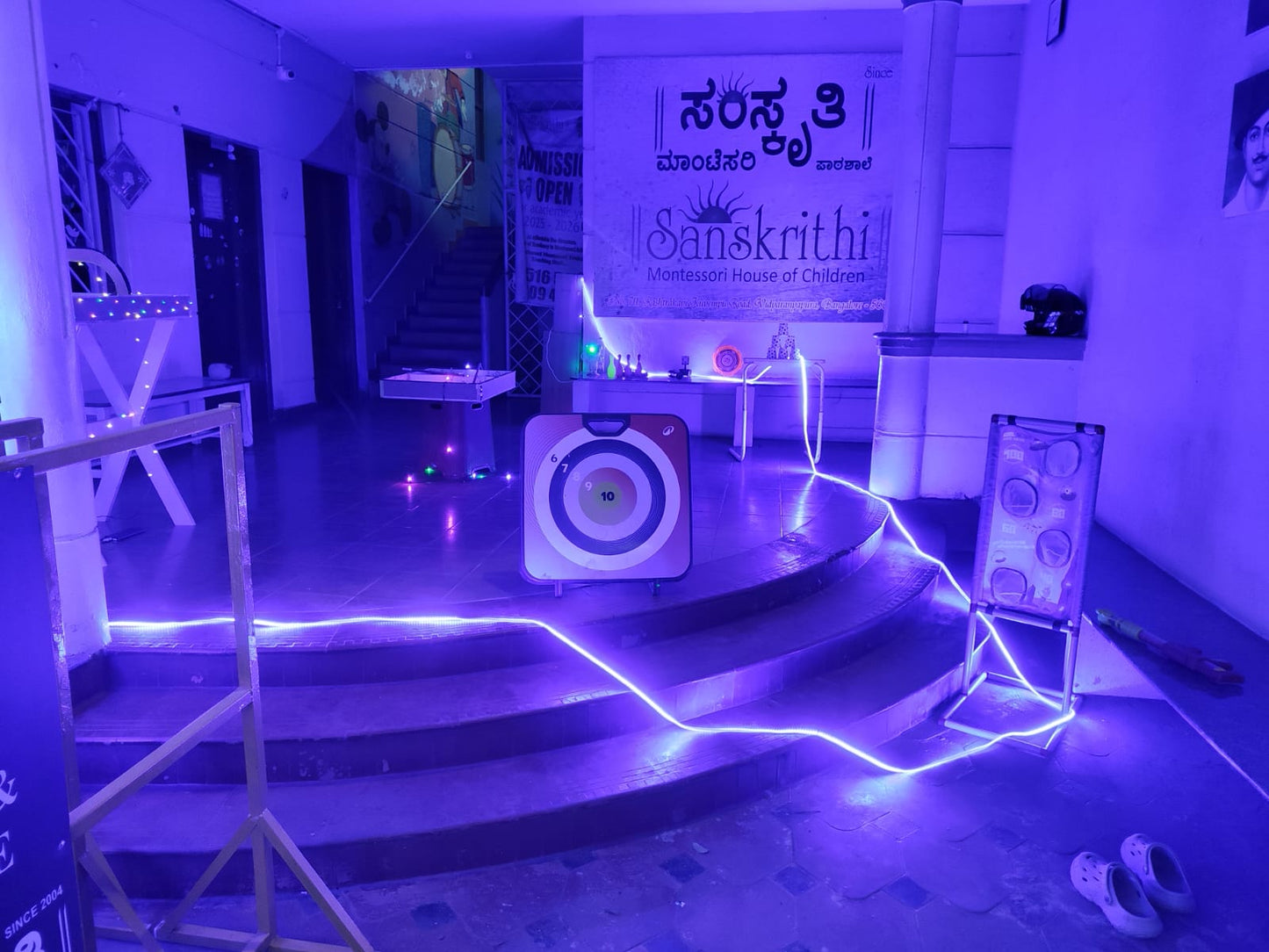 A dimly lit indoor space with blue neon lights, featuring a target game and a banner for a children's Montessori school.
