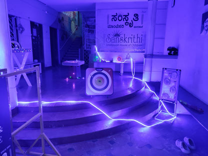 A dimly lit indoor space with blue neon lights, featuring a target game and a banner for a children's Montessori school.