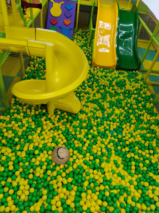 A ball pit filled with yellow and green balls, featuring slides and a woven hat.