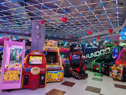 Indoor gaming arcade with bright machines and heart-shaped balloons under a glowing grid ceiling at Fundoo Gaming Zone Rohini