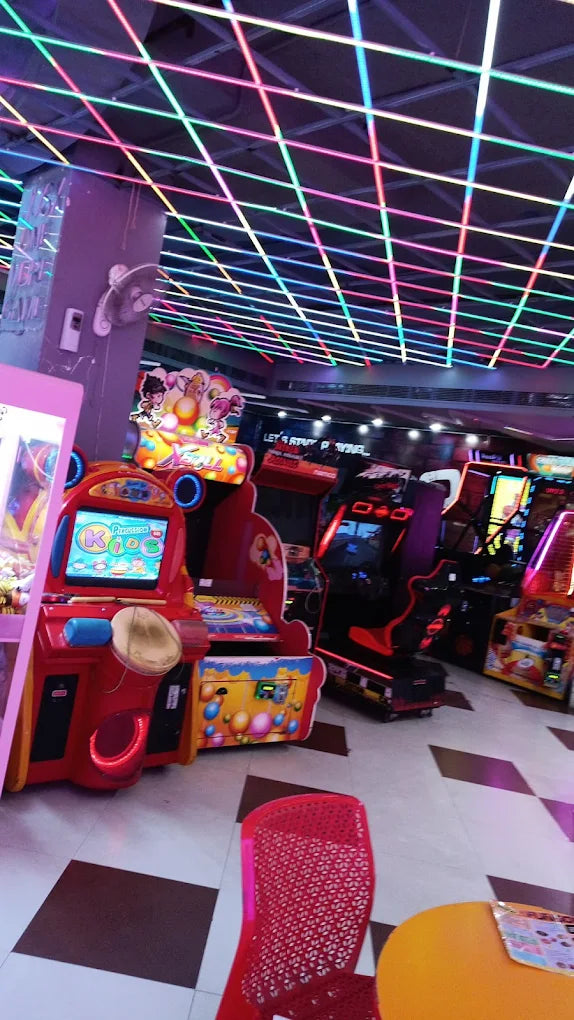 Indoor arcade featuring colorful kids and racing games under a vibrant neon grid ceiling lighting setup