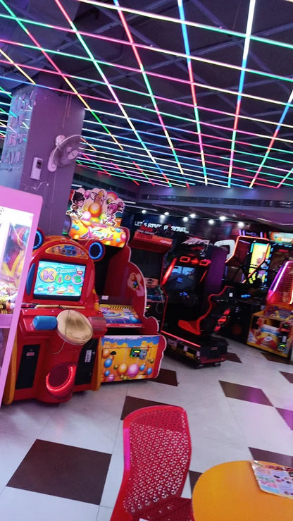 Indoor arcade featuring colorful kids and racing games under a vibrant neon grid ceiling lighting setup