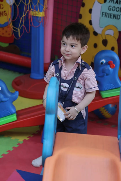Toddler standing near a blue seesaw with colorful play mats and playful equipment in a cheerful indoor play area