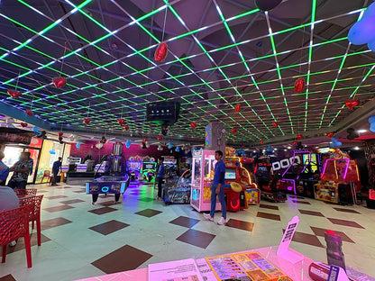 Vibrant indoor gaming zone with various arcade machines and neon grid ceiling lighting in a colorful play area