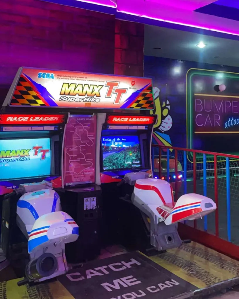 Retro motorcycle racing arcade games with white and red blue bikes in an indoor gaming area lit with purple neon lights