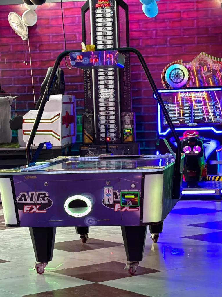 Air hockey table with digital scoreboard in a colorful indoor game zone featuring neon lights and arcade machines