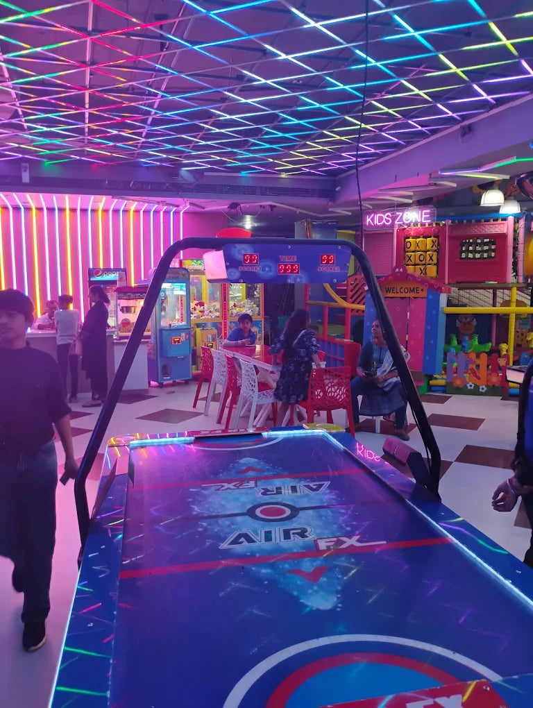 Indoor amusement center with air hockey table, vibrant neon lighting, and children enjoying various arcade games and play areas