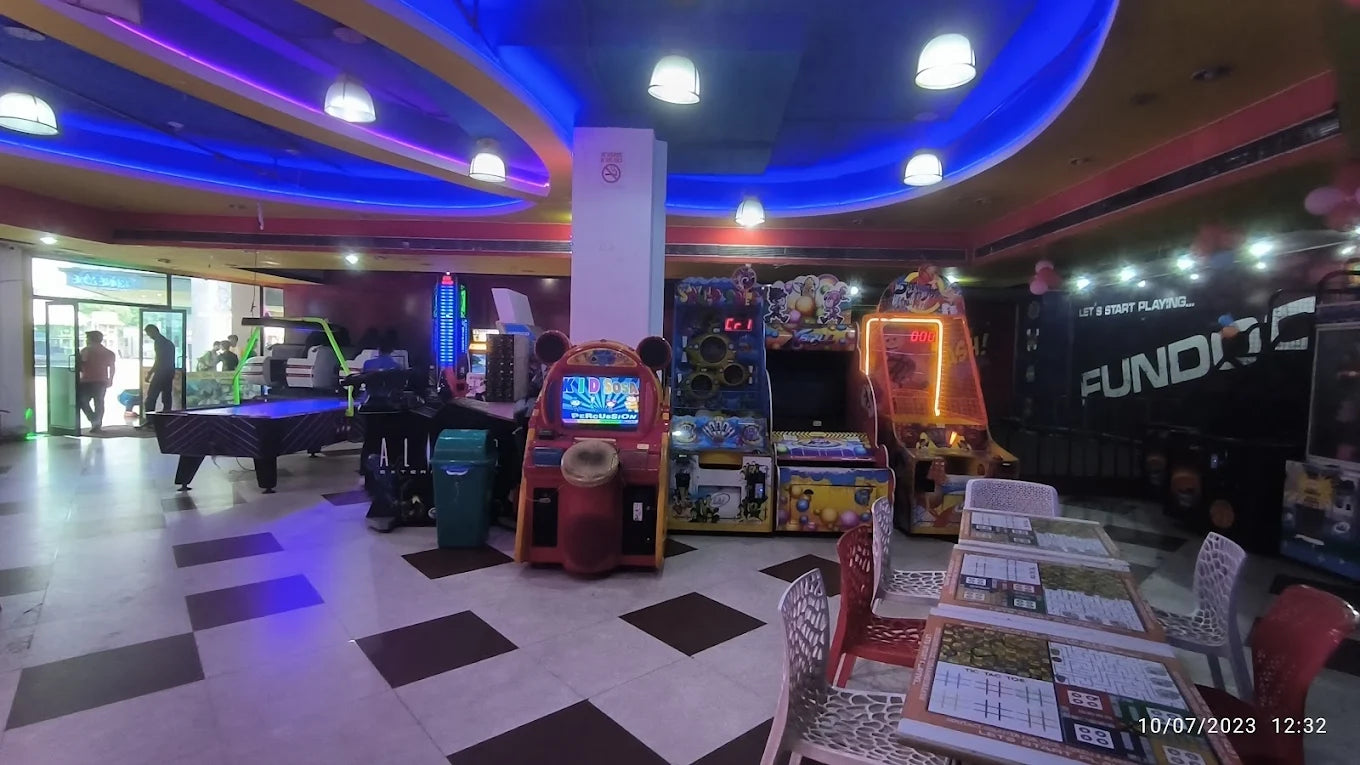 Spacious indoor gaming center with arcade machines, pool table, and seating area under colorful ceiling lights