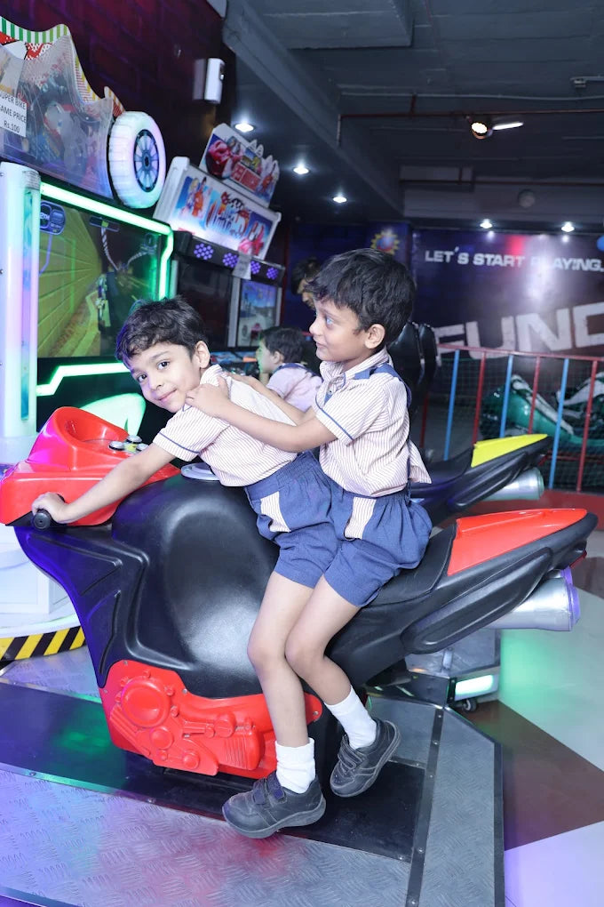 Two boys playing on a motorbike simulator game in a lively indoor gaming zone with vibrant lighting and arcade machines