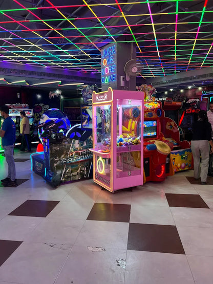 Indoor gaming arcade with neon-lit claw machine, racing simulators, and colorful arcade games in a lively entertainment space