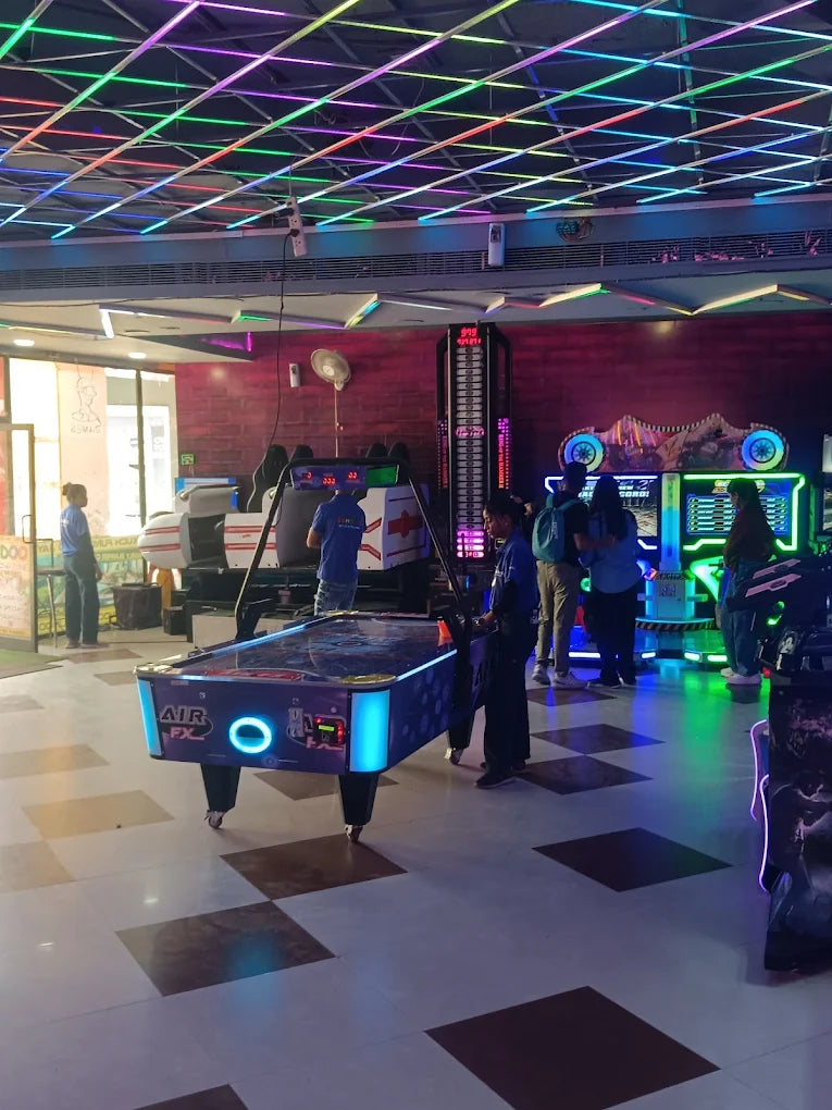 Indoor gaming area with air hockey table and arcade machines under colorful LED ceiling lights and vibrant atmosphere