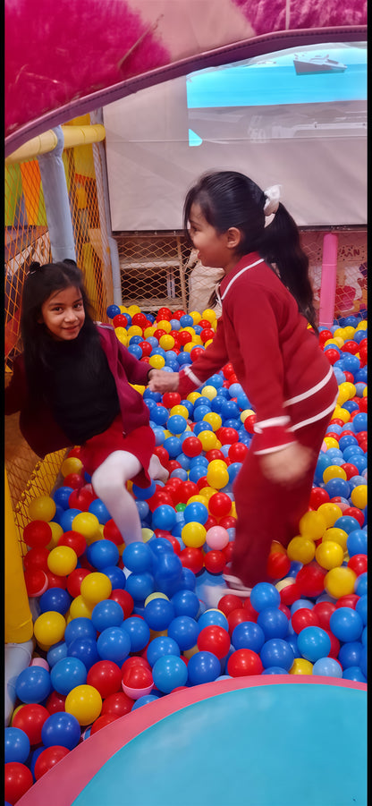 Two children playing in a colorful ball pit with a pink archway.