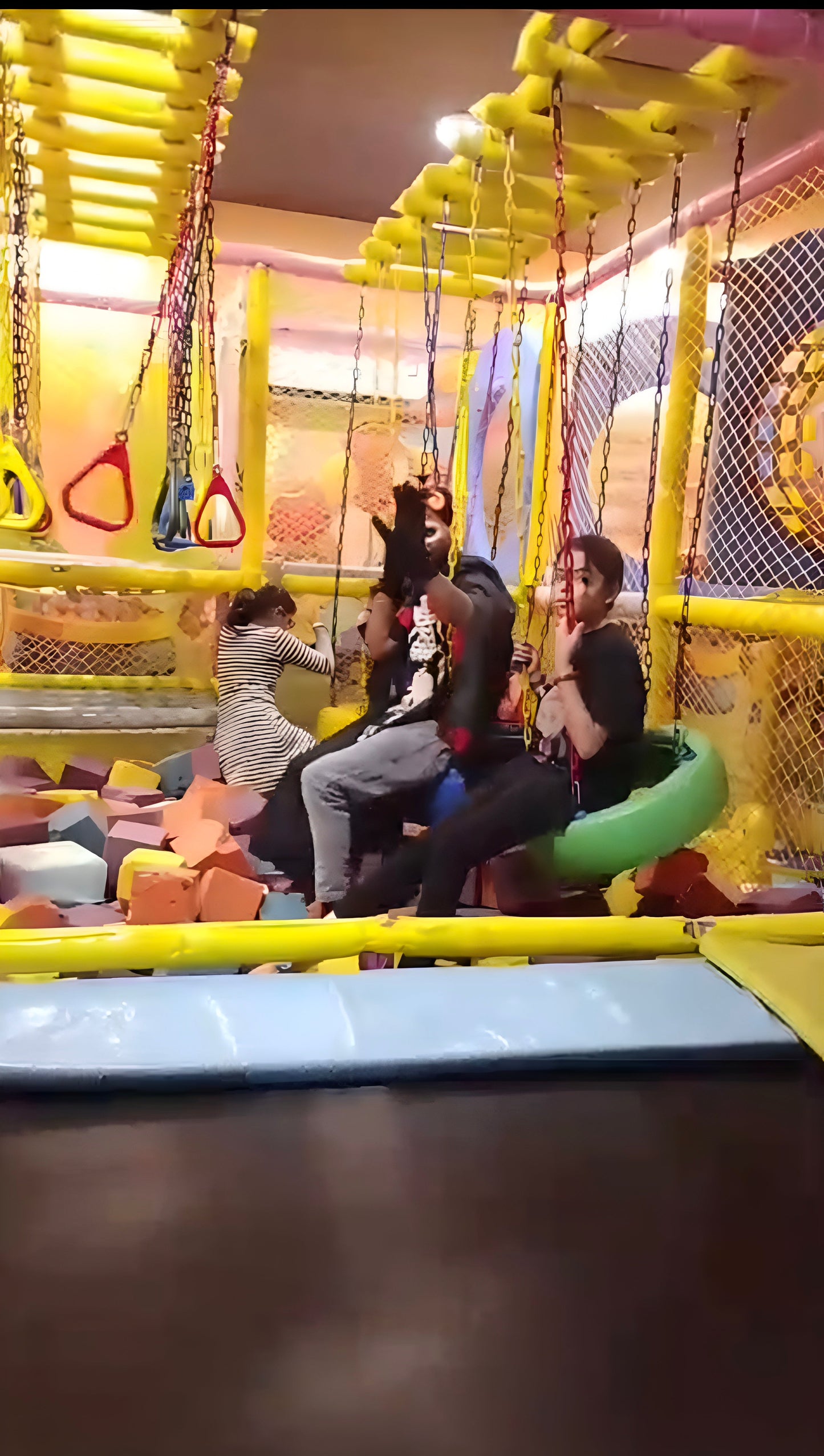 Children playing in a colorful indoor playground with slides and swings.